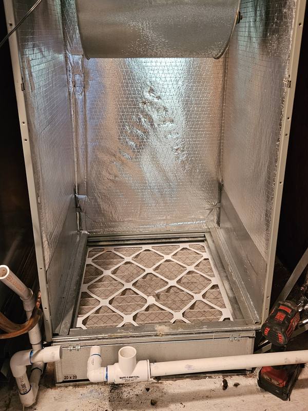 Air handler opened up during an evaporator coil replacement, with the old coil removed, the blower above and the drain lines with a safety float switch below